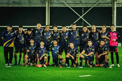 Equipo juvenil de fútbol de Cali Leones posando con sus entrenadores en cancha sintética